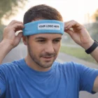 Man in blue shirt adjusts a HeadBands headband labeled YOUR LOGO HERE outdoors.