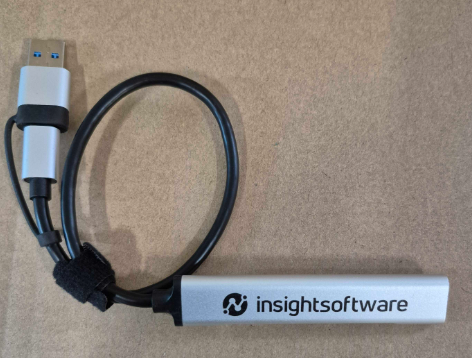 A USB cable with a silver insightsoftware branded adapter on a brown surface.