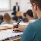 Student uses Corporate Metal Stylus Pen to take notes in a lecture hall with teacher and classmates.