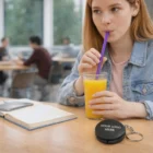 Woman sips juice with a reusable straw and keyring case on the table.