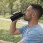 Man in blue shirt drinks from a 350Ml Logo Branded Eclipse Coffee Cup while sitting in the park.