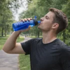 Man drinks from The Basic Promotional 725ml Bottle while standing on a park path.
