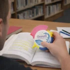 Person highlighting a textbook with Triple Logo Imprinted Highlighters in hand.