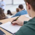 Student writing notes with Giro Stylus Pens With Logo Decoration in a classroom.