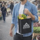Man holding a black AXIOM bag and an Express Kraft Paper Bag Small at an outdoor market.