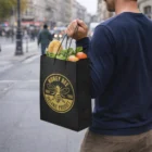 Person holding an Express Kraft Paper Bag Medium filled with produce, featuring a logo.
