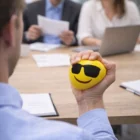 Person squeezes a Yellow Emoji Stress Ball at a meeting table.