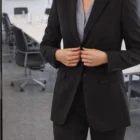 Woman in a dark suit buttons a Premium Womens Mid Length Jacket in an office setting.