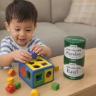 A toddler plays with the Magic Cans Shape beside stacked herb containers on the table.