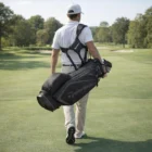 Man in white carries a Taylormade Select Black Grey Stand Bag on a sunny golf course.