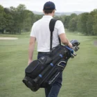 Man carrying a Taylormade Premium Black Blue Cart Bag over his shoulder on the golf course.