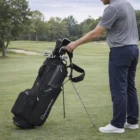 Person on grass beside a Taylormade Flextech Black Grey Stand Bag on a golf course.