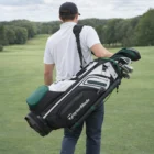 Man carrying a Taylormade Premium Black White Green Cart Bag on a tree-lined golf course.