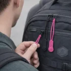 Person holding Classic Zip Pullers Accessories in pink on a black backpack worn by someone else.