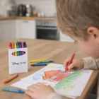 Child colors a house drawing with Brillantblend Crayon Sets at a kitchen table.