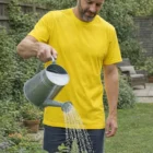 Man in yellow Mens Everyday Tee watering garden plants with a metal watering can.