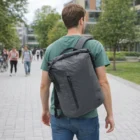 A person walks outside in a green shirt with a gray Stormtech Teton Roll-Top Backpack.