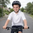 A smiling boy in a Poly Cotton Kids Polo and helmet rides his bike on a quiet street.