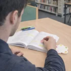 Person using Skien Flower Sticky Notepads while highlighting a textbook at the library desk.