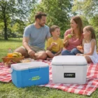 A family picnics on a red blanket with food and Gage 6L Lightweight Cooler Boxes in the park.