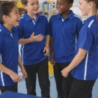 Four kids in Kids Dry Short Sleeves Contrast Polos smile and chat with music sheets and a tambourine.