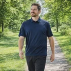 Man in Stormtech Mens Eco Performance Short Sleeve Polo walks on a sunlit path in a park.