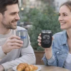 A man and woman toast Gandia Double Wall Curved Mugs at a table with croissants.