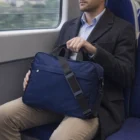 Man in coat holding a Hartford Corporate 600D Polyester Briefcase while on a train.