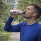Man in blue shirt drinks from Hydratepro 600ml Aluminum Bottle with NETFLIX label on path.