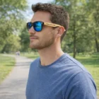 Man in blue shirt wearing Nas Bamboo Sunglasses with custom logo on arm, outdoors.