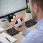 Person squeezing a Jumbo Soccer Ball 130MM stress toy at their desk with computer and coffee.