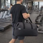 Man carrying a Swissdigital Arosa Duffle Bag in a gym with treadmills and equipment.