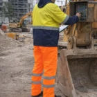 Construction worker in Hi-Vis Pants operates machinery at a building site.