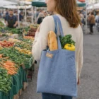 Woman at farmers market with a Betty Recycled Cotton Tote Bag filled with bread, kale, and pepper.
