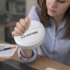 Woman holding a white Stress Toy Tablets at a desk with papers and a laptop.