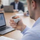 Person holding a Coffee Cup Stress Toy at a meeting table with laptop and documents.