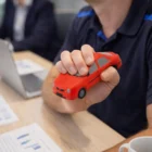 Person holding a Stress Toys Sedan at a desk with papers, laptop, and coffee cup.