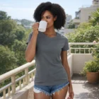 Woman wears Womens Classic Organic Cotton Tee and denim shorts, sipping from a mug on sunny balcony.
