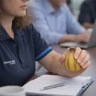 Person holding a yellow Stress Toy Onions while taking notes at a meeting table with others.