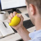 Person squeezing a Stress Balls Lemon for stress relief at a desk with a computer.