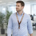 Man in blue shirt wearing a brown Satin Lanyard labeled YOUR LOGO HERE in an office.