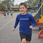 Smiling boy in Patriot Corporate L/S Tee runs on playground near slide and other children.