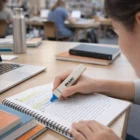 Person highlighting text in a notebook with Bowie Eco Highlighters at a library desk.