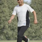 Smiling child dribbling a soccer ball in Unisex Cooldry Expo T Shirts Kids on a grassy field.