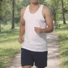 A man in Mens Cotton Corporate Singlet T Shirts jogging on a park trail with greenery.