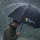 A person holds an Articus Fibreglass Golf Umbrella in heavy rain, wearing a hooded jacket.