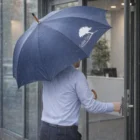 A person enters a building on a rainy day holding an Executive Umbrellas.