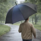 A person walks in a lush park with Extra Large Promotional Umbrellas on a wet path.