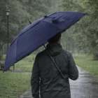 Person walks in a park on a rainy day, holding a 60-Inch Vented Tipless Ends Golf Umbrella.