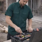 Man wearing a Cotton Drill Work Shirt-Short Sleeves organizes tools in a black toolbox on site.